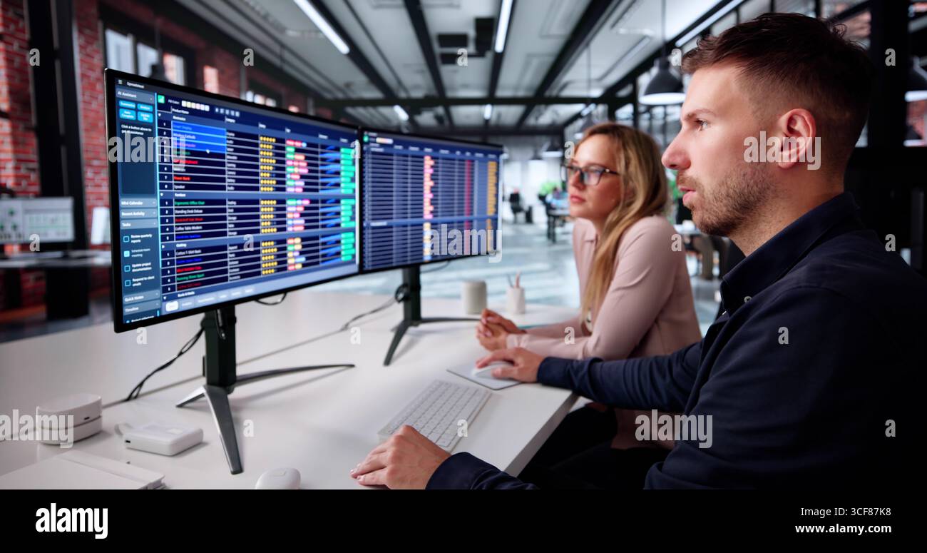 Man And Woman Study Spreadsheets On Computer In Office. Stock Photo