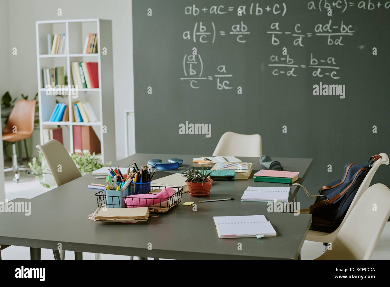 Empty Classroom with School Supplies on Table and Math Equations on Chalkboard Stock Photo
