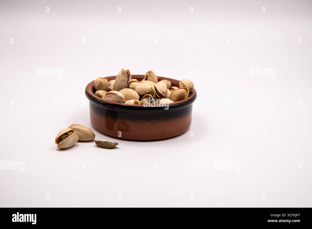 Small terracotta dish filled with pistachio nuts on a clean white background, perfect for illustrating healthy snacks, nutrition, and natural food Stock Photo
