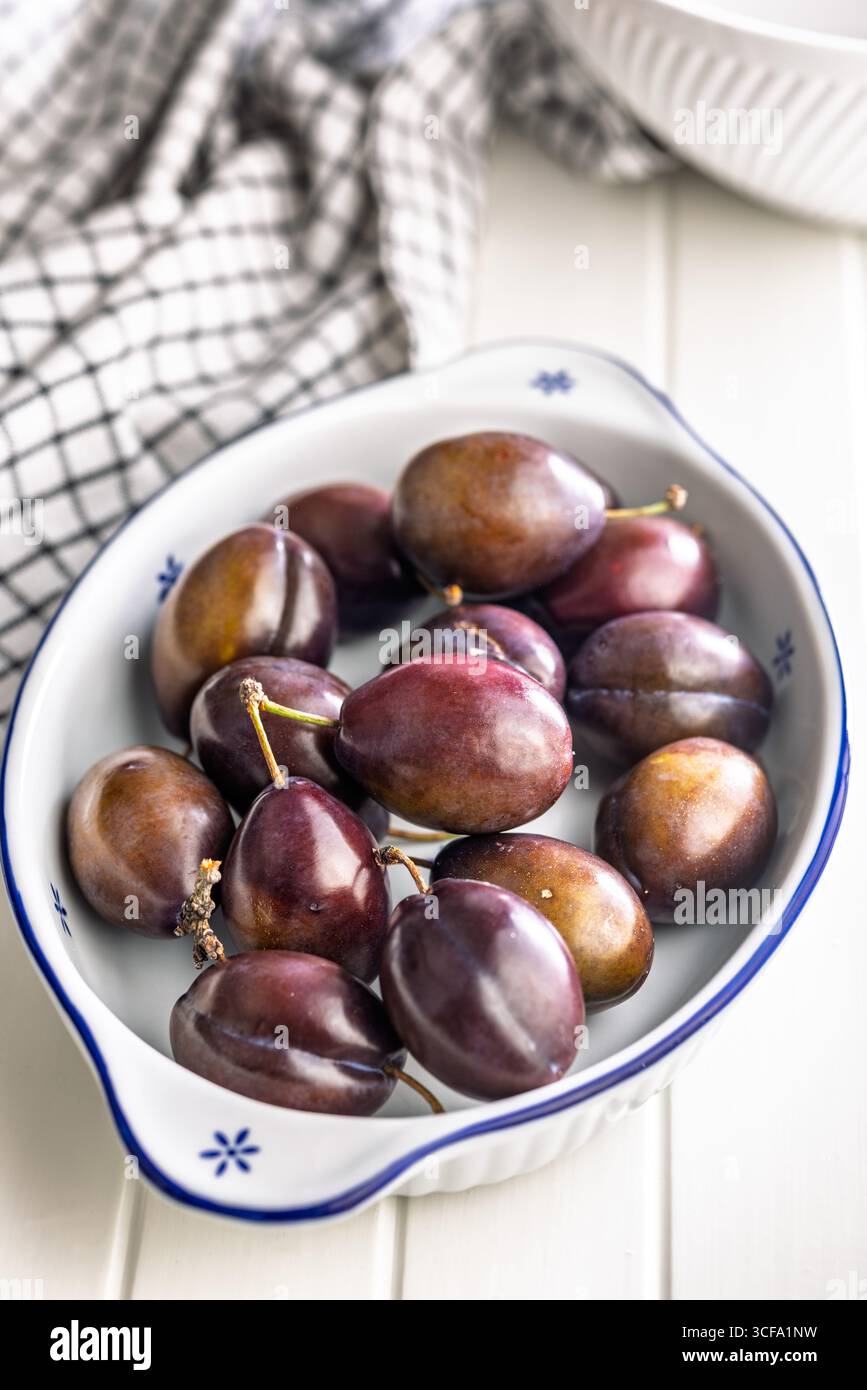 Ripe plums in bowl on a white table. Stock Photo