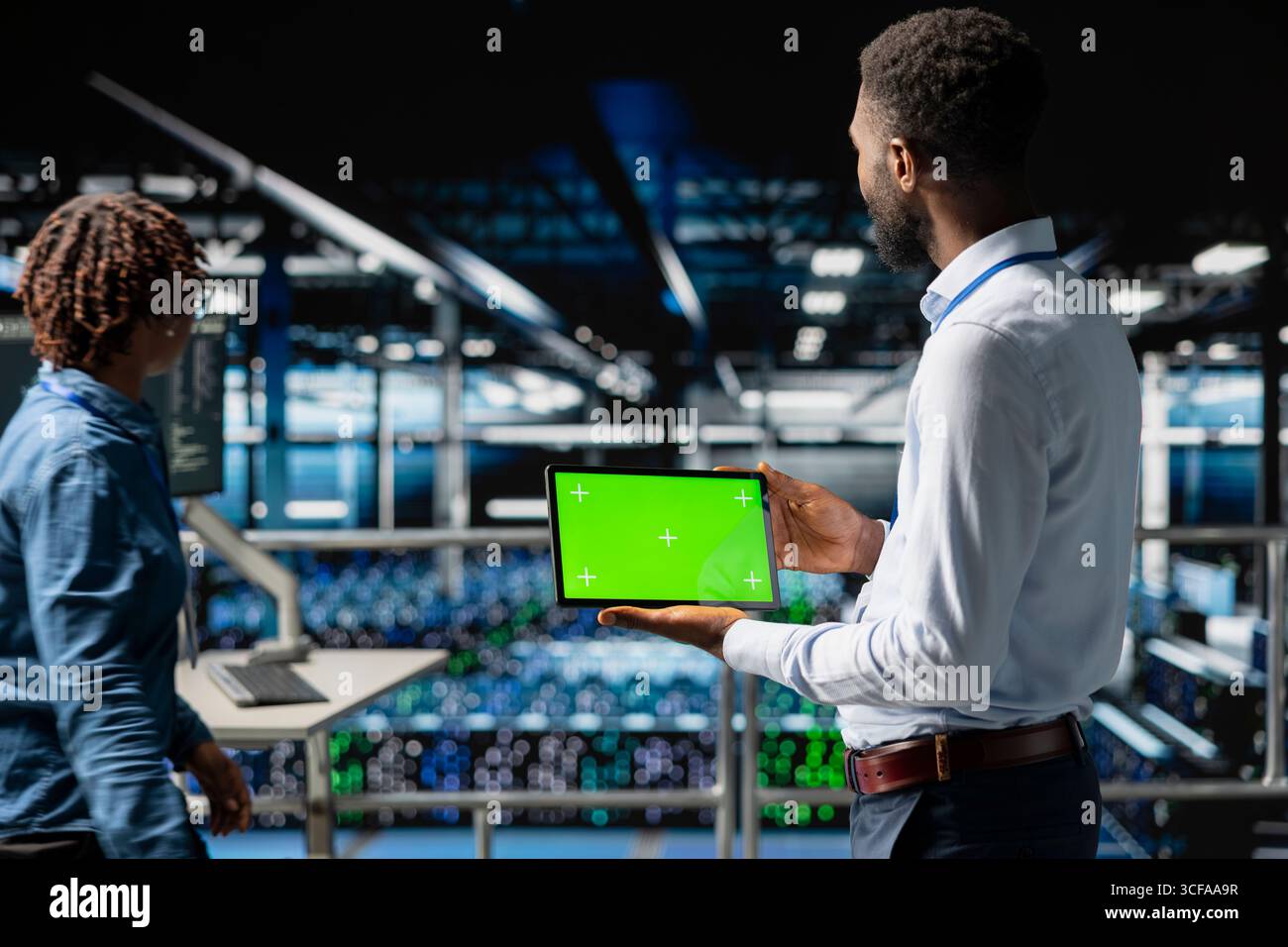 Data center programmer on industrial platform using green screen tablet, solving optimization tasks around the server farm. Male worker visualizing system performance using mockup screen. Stock Photo