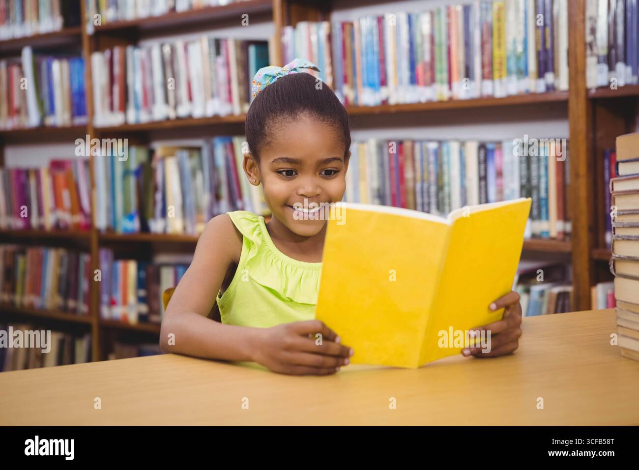 African American girl sitting at wooden table reading yellow book with ...