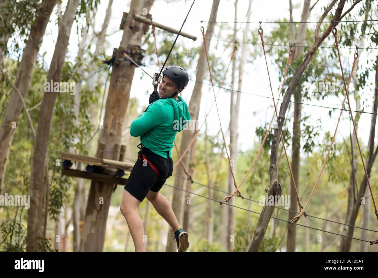 Man wearing helmet and harness navigating high-rope cables and ...