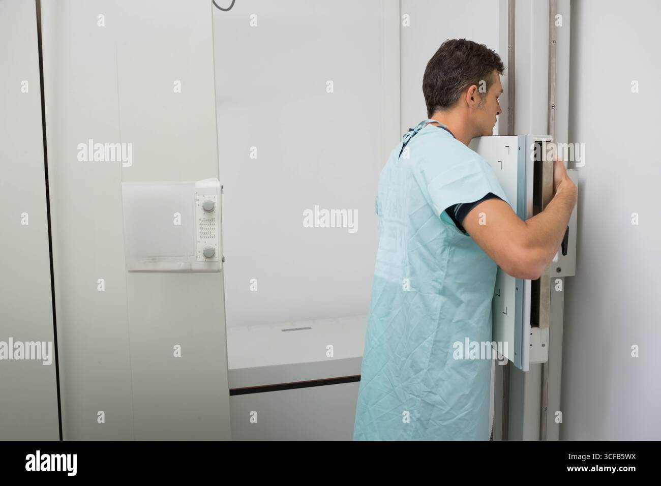 Radiology technologist adjusting digital X-ray detector on stand at imaging table in radiology room Stock Photo