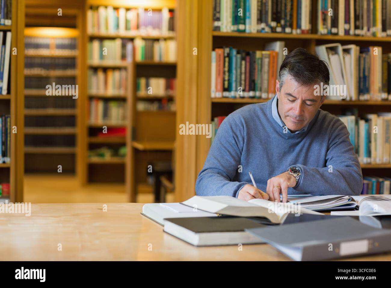 Mature adult man writing notes in spiral notebook at reading room with ...