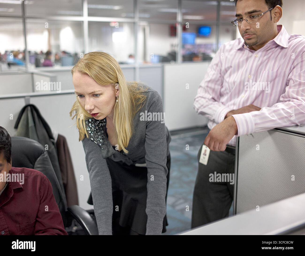 Two workers peering over the shoulder of their coworker. Stock Photo