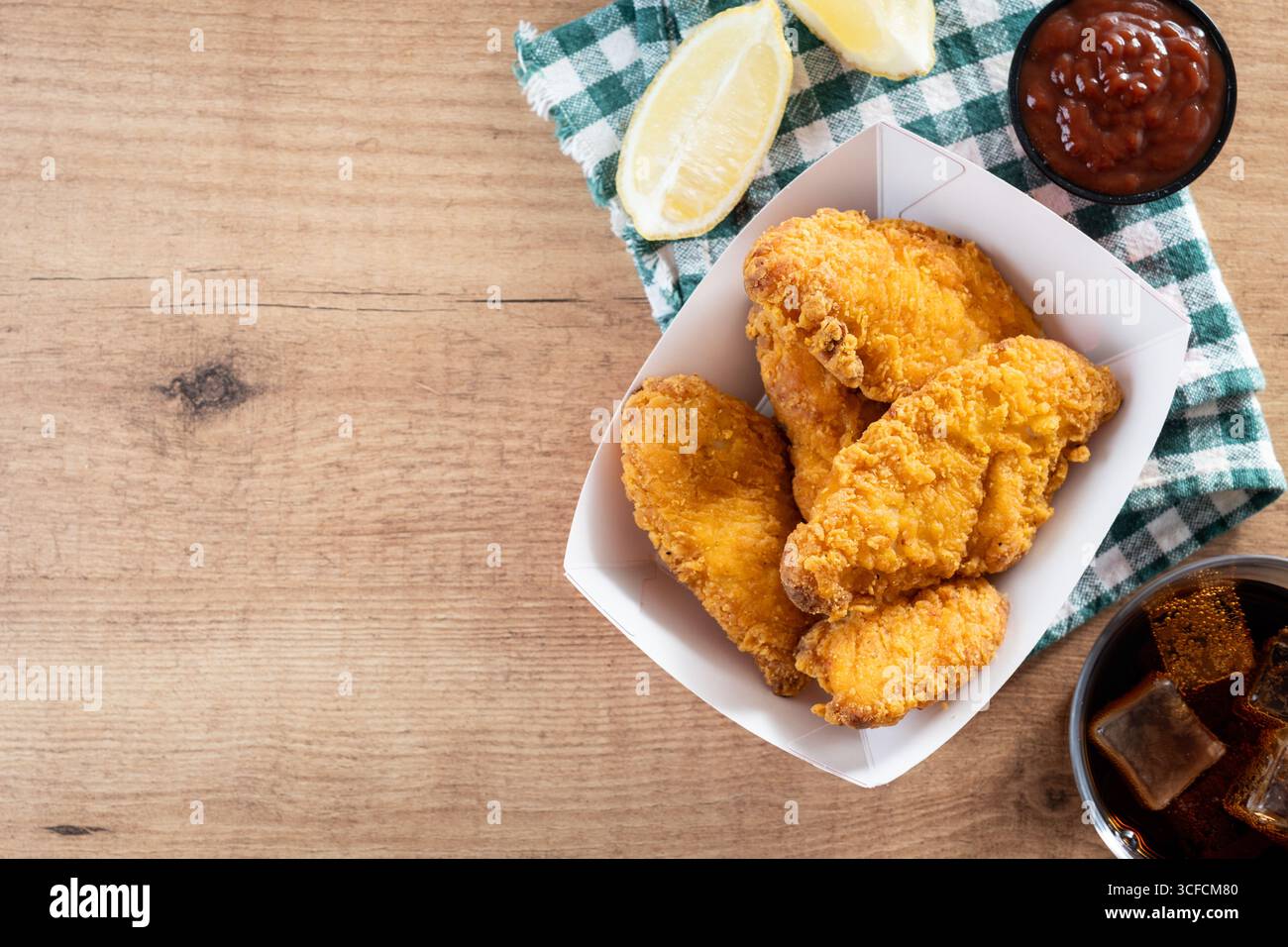 Close-up of golden crispy fried chicken tenders served in a red and white paper tray on wooden table. Stock Photo