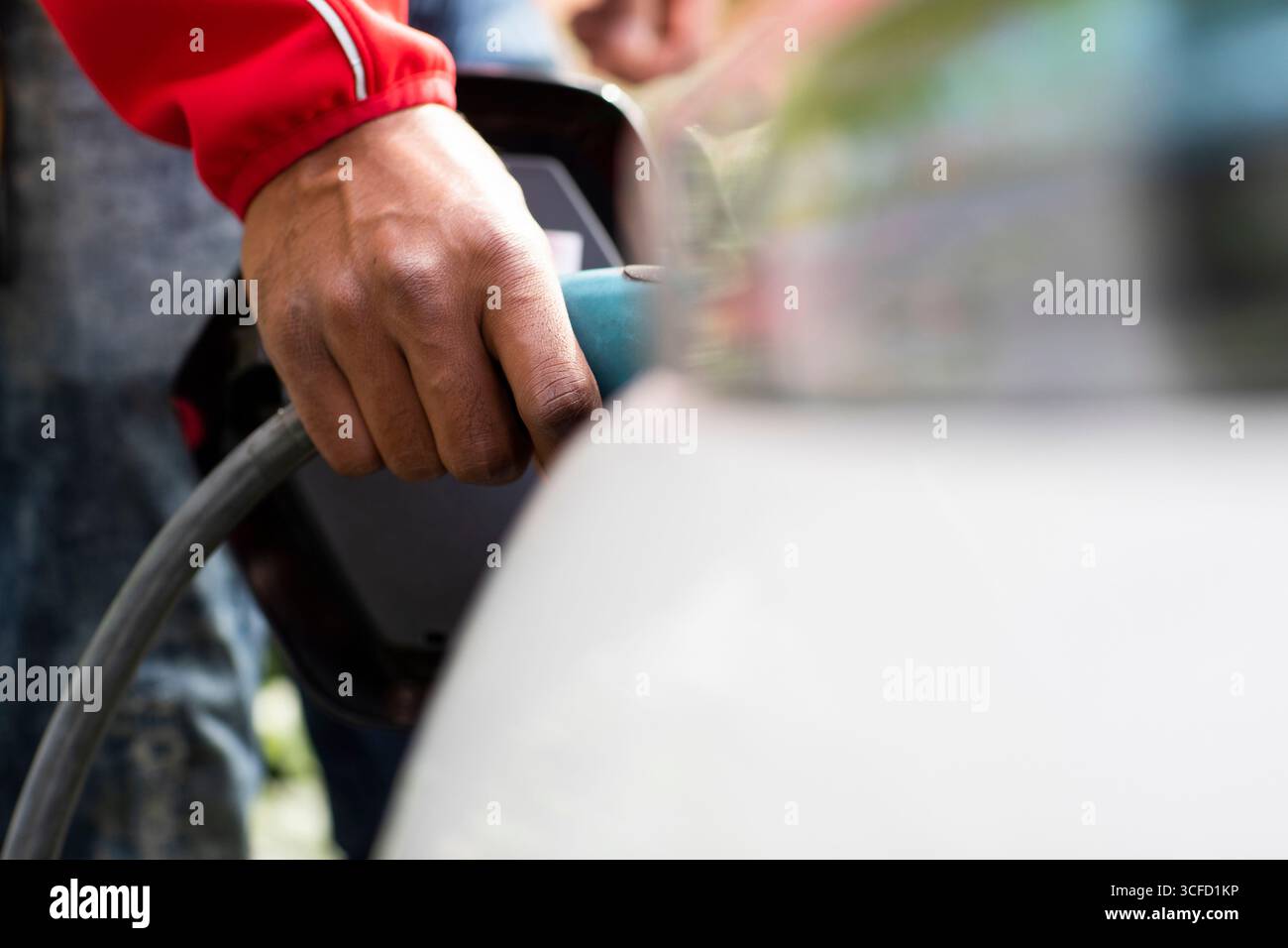 Hand in red sleeve plugging cable into electric car for charging. Germany Stock Photo