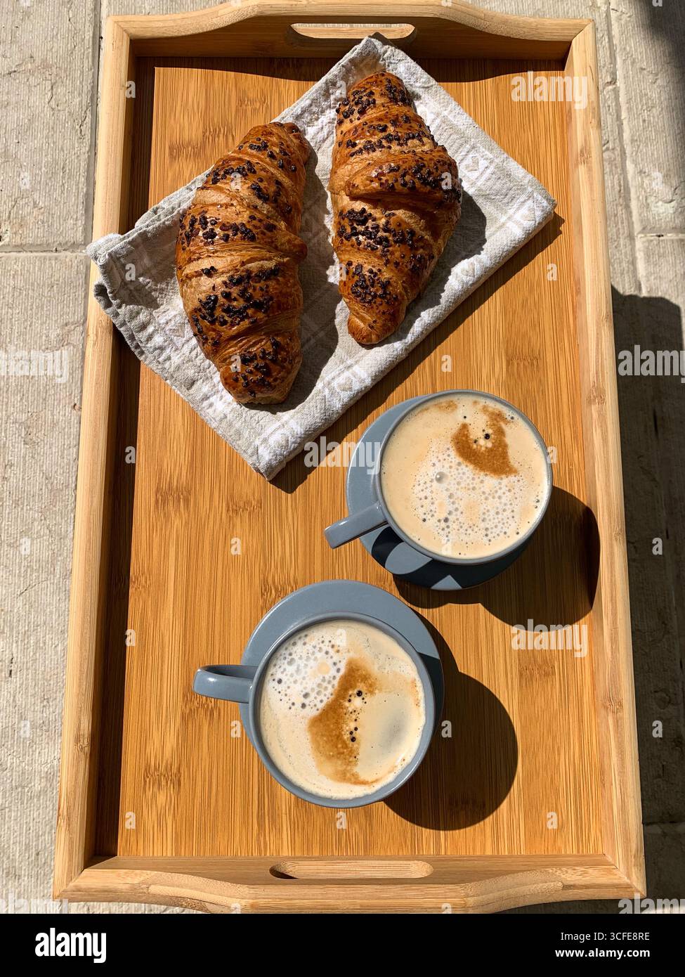 Traditional Italian breakfast. Fresh croissants and cappuccino on a wooden tray. View from above. European food and pastry. Morning meal and cozy home - Smartphone Captured Stock Image