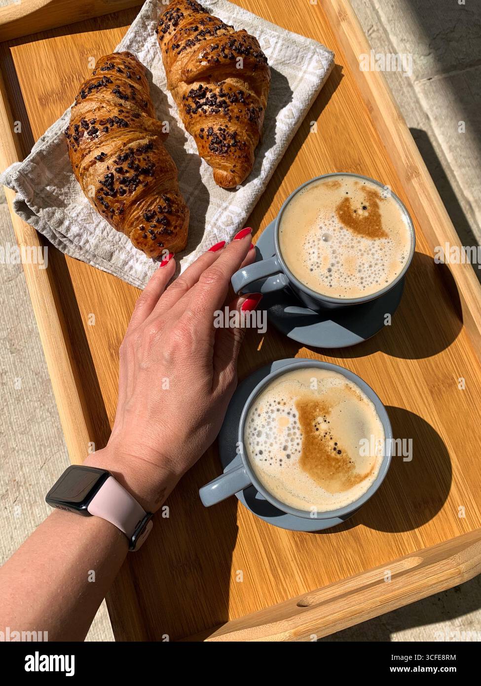 Traditional Italian breakfast. Fresh croissants and cappuccino on a wooden tray. Woman's hand holding a cup of Cappuccino, view from above. - Smartphone Captured Stock Image