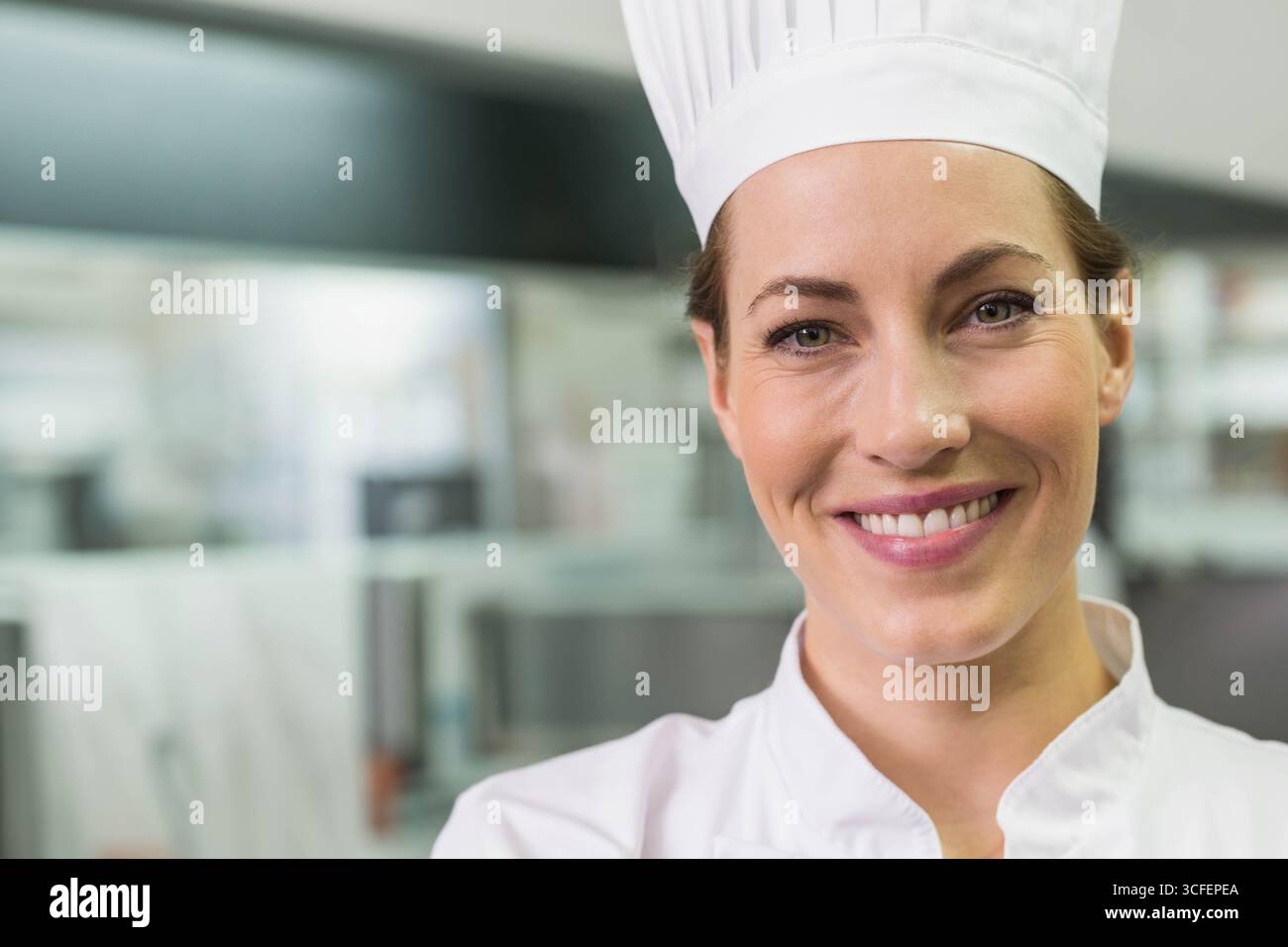Female chef standing in commercial kitchen with counters wearing chef ...