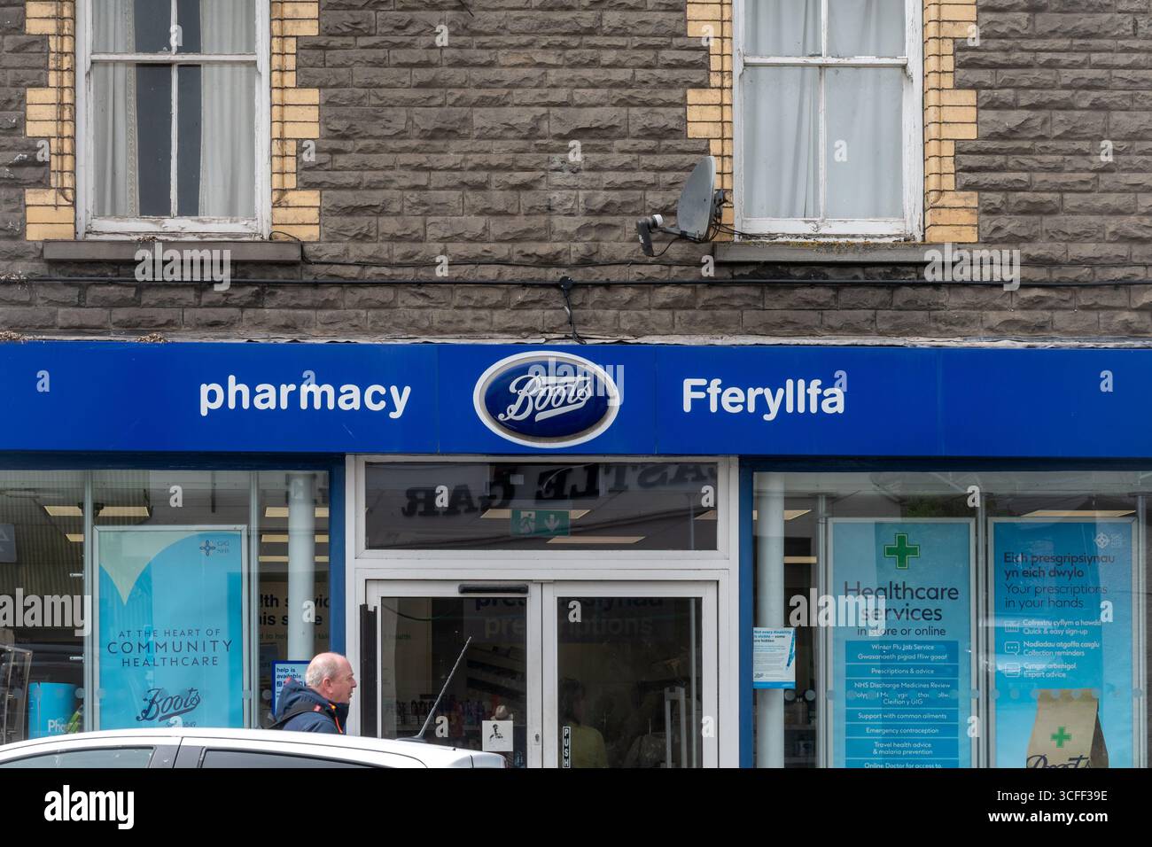 Man walking past Boots Pharmacy in Wales, with bilingual sign, Welsh language Fferyllfa Stock Photo