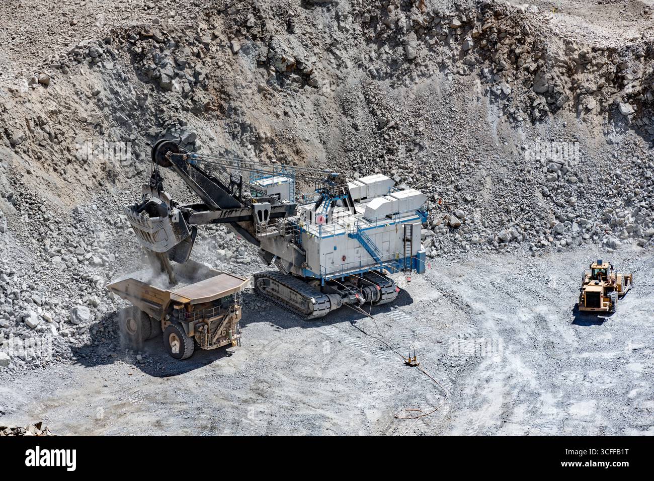 A large excavator loads a massive haul truck at an open-pit copper mine in Chile, showcasing the scale of the operation. Stock Photo
