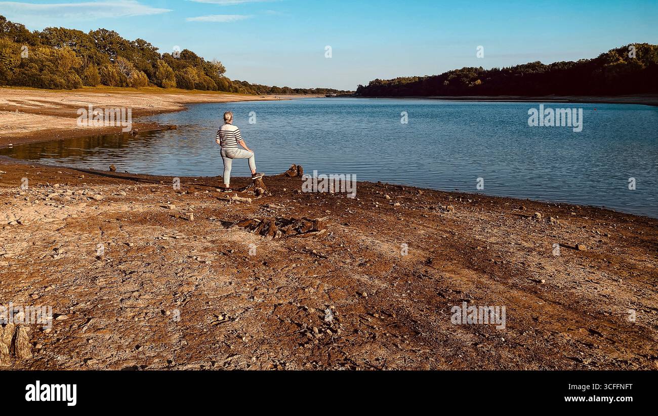 Ardingly Reservoir in West Sussex. 22nd Aug 2025, Barren and dry reservoir, female looking onto a nature reserve after the hottest summer on record UK - Smartphone Captured Stock Image