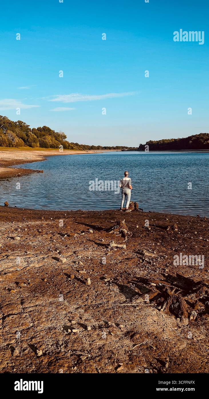 Ardingly Reservoir in West Sussex. 22nd Aug 2025, Barren and dry reservoir, female looking onto a nature reserve after the hottest summer on record UK - Smartphone Captured Stock Image