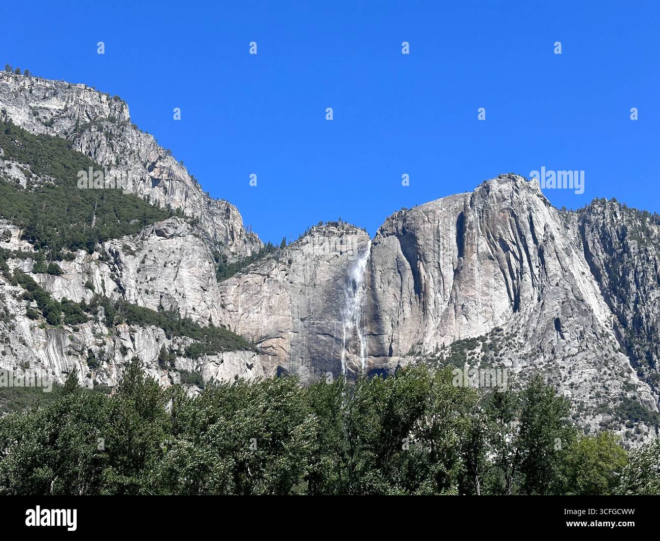 Scenic view of Yosemite Falls cascading down granite cliffs in Yosemite National Park, California, USA. The clear blue sky, and forested valley - Smartphone Captured Stock Image