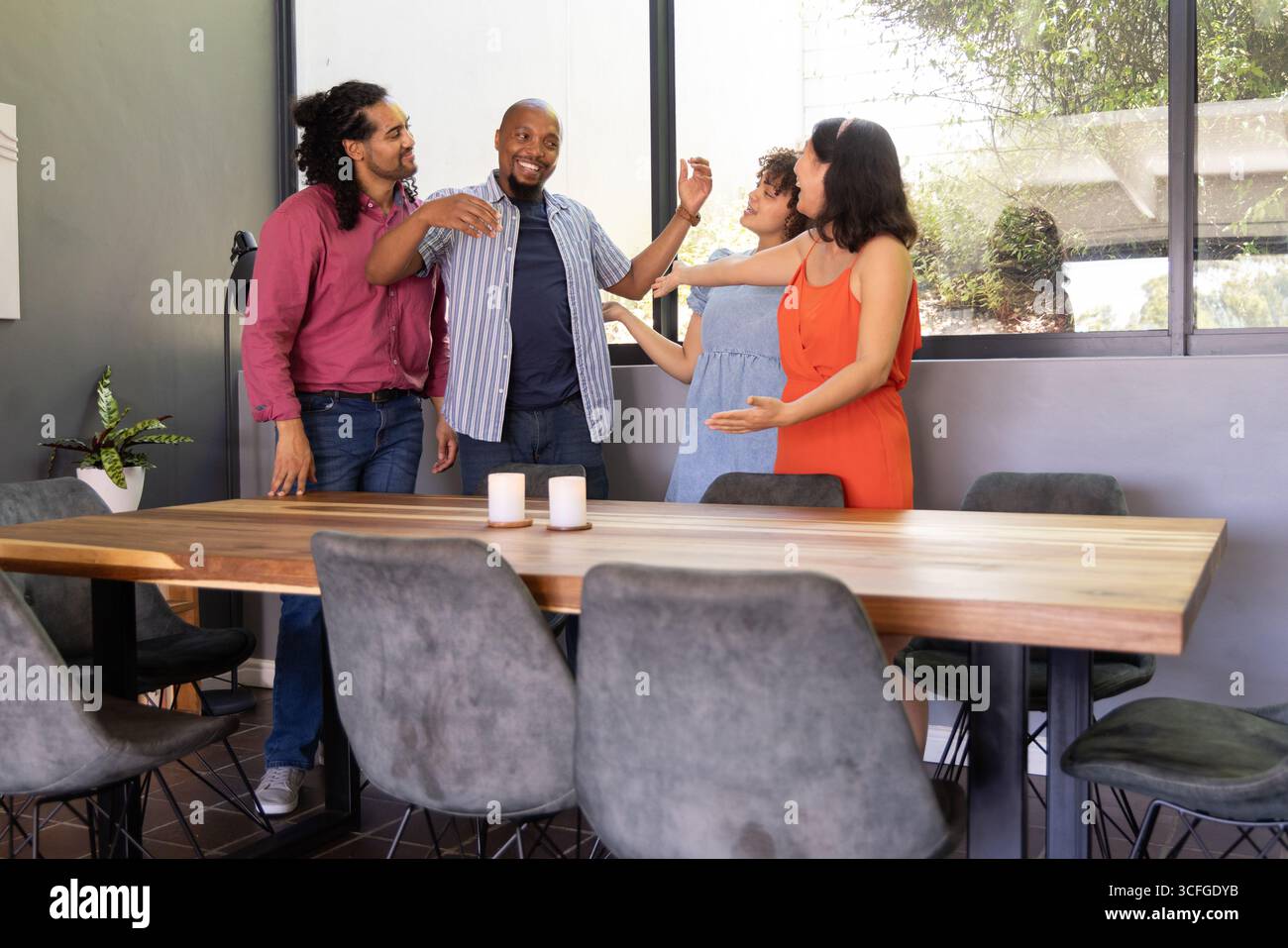 Diverse coworkers smiling and extending arms in group hug around table ...