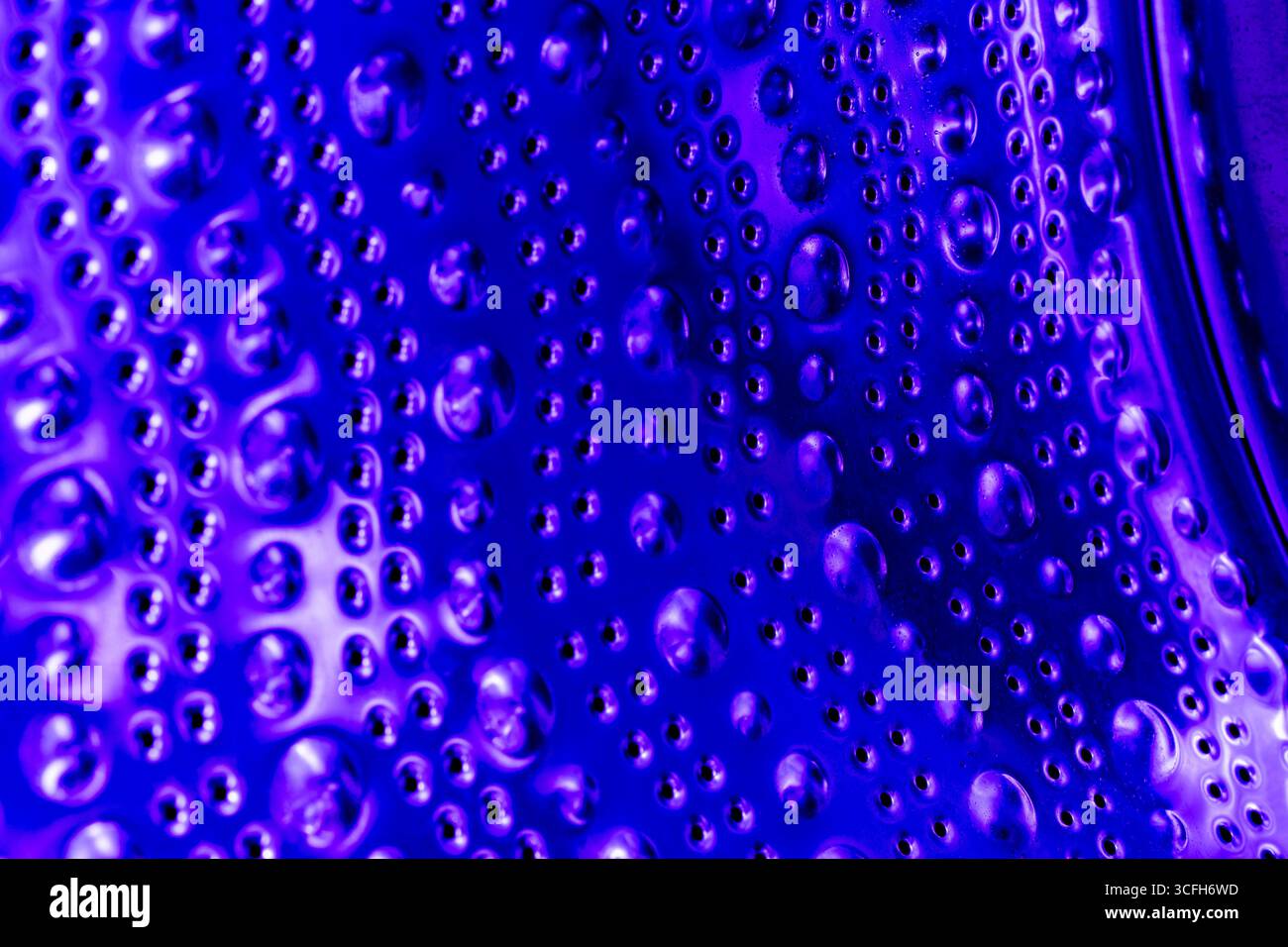 Empty washing machine drum inside in blue light, close up view. Metal dots and bubbles as abstraction and background Stock Photo