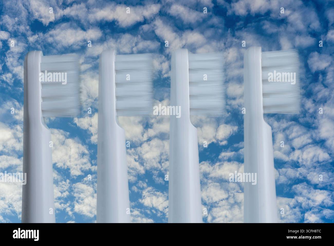 Four white plastic toothbrushes on a blue sky background, close up Stock Photo