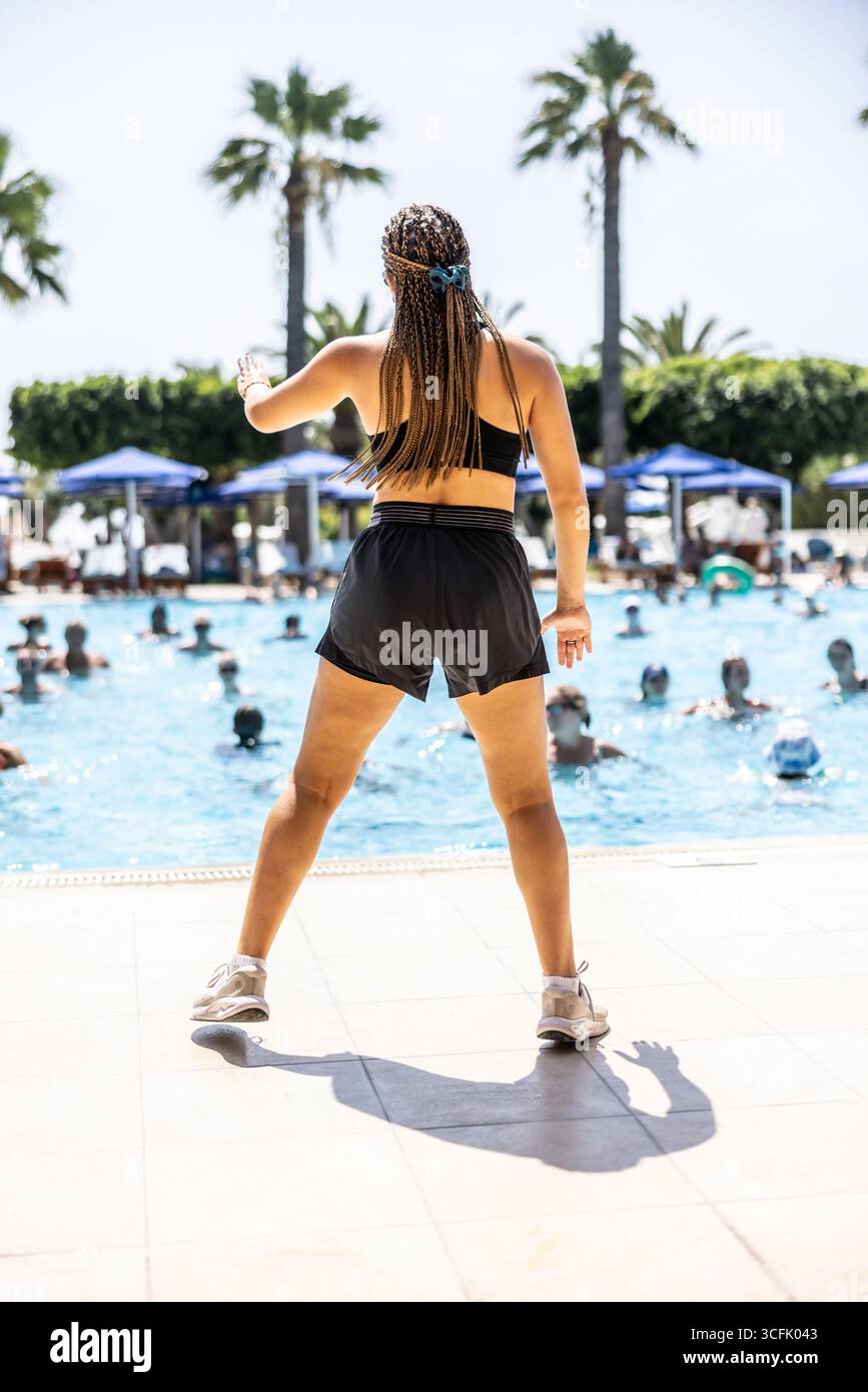 A young female Sports Animator is doing water aerobics for people in the pool of a hotel resort. Stock Photo