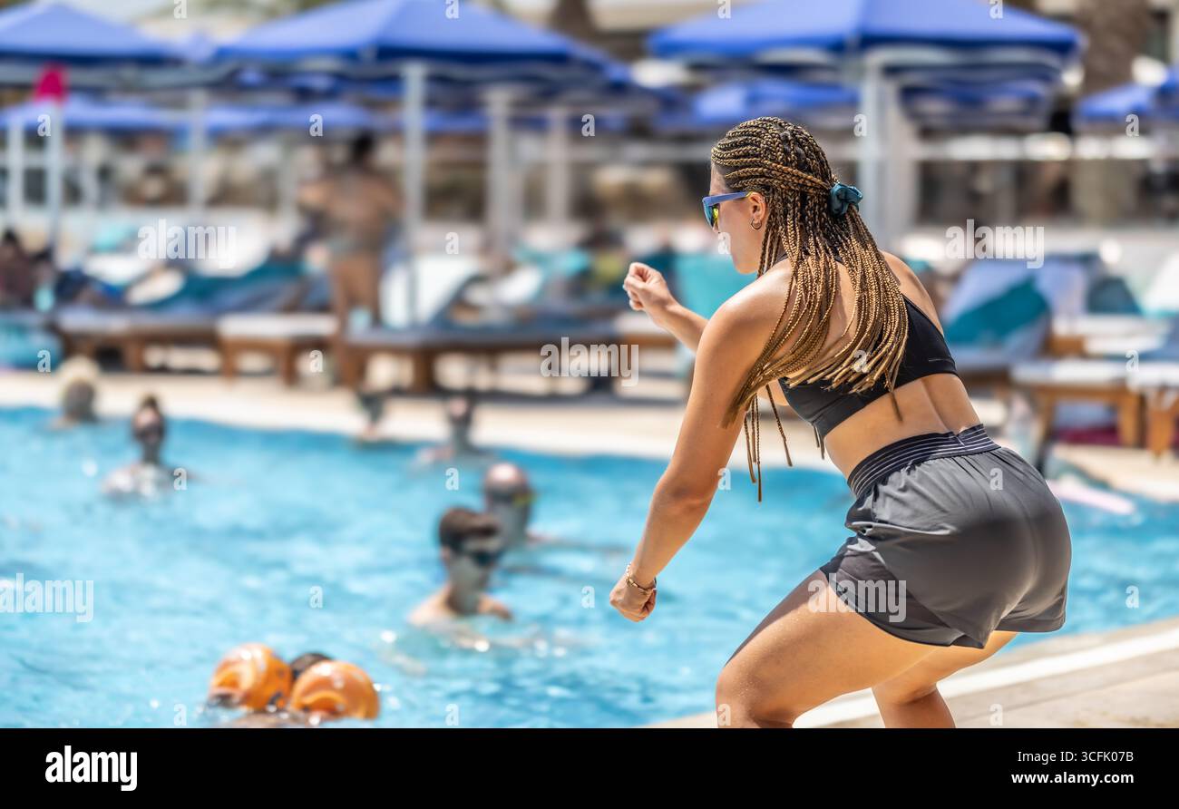 A young female Sports Animator is doing water aerobics for people in the pool of a hotel resort. Stock Photo