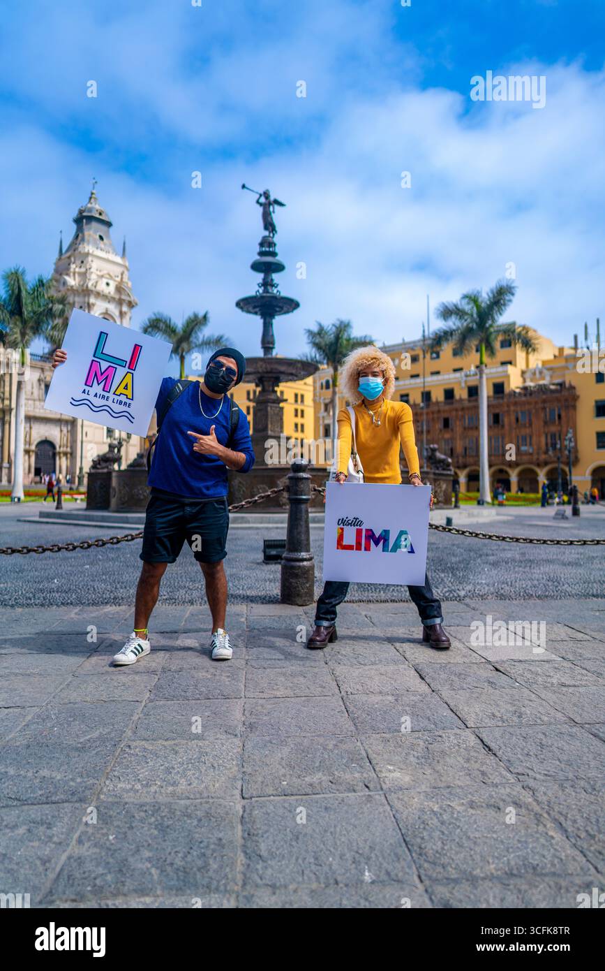 People holding Lima al Aire Libre and Visit Lima signs at Plaza Mayor of Lima Peru, promoting safe tourism and urban cultural events. Stock Photo