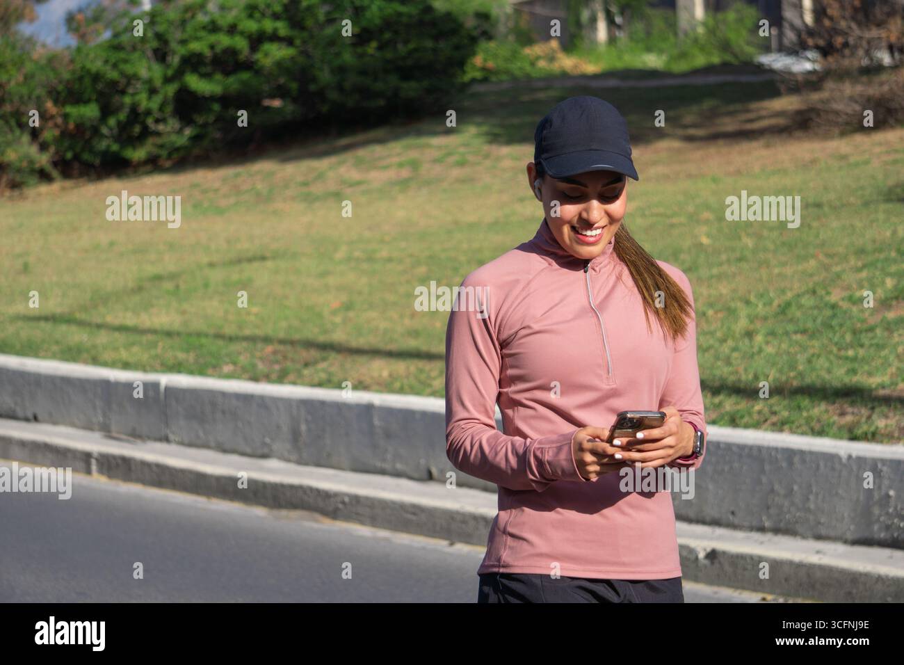 Young Latina woman checking her phone while walking outdoors Stock Photo