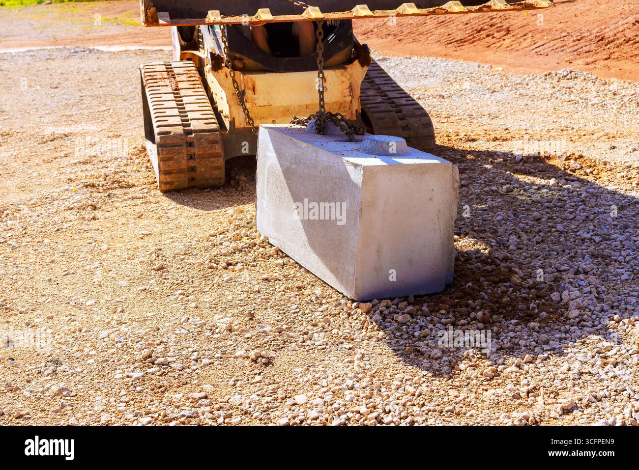 Construction vehicle carefully lifts places concrete block onto gravel ...