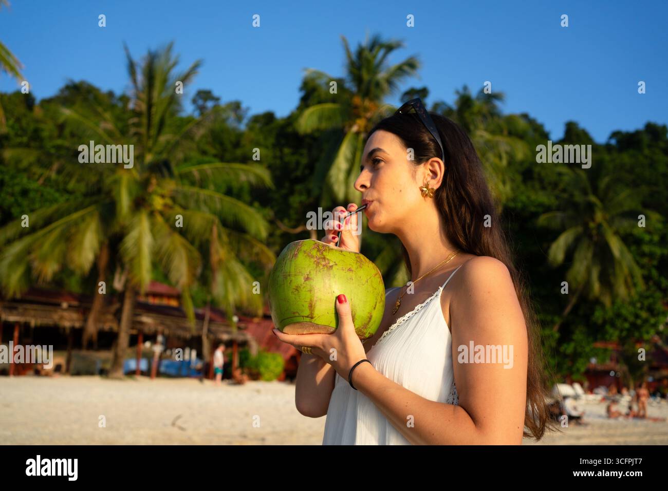 Young woman enjoying a refreshing coconut on a beautiful beach in the tropics Stock Photo