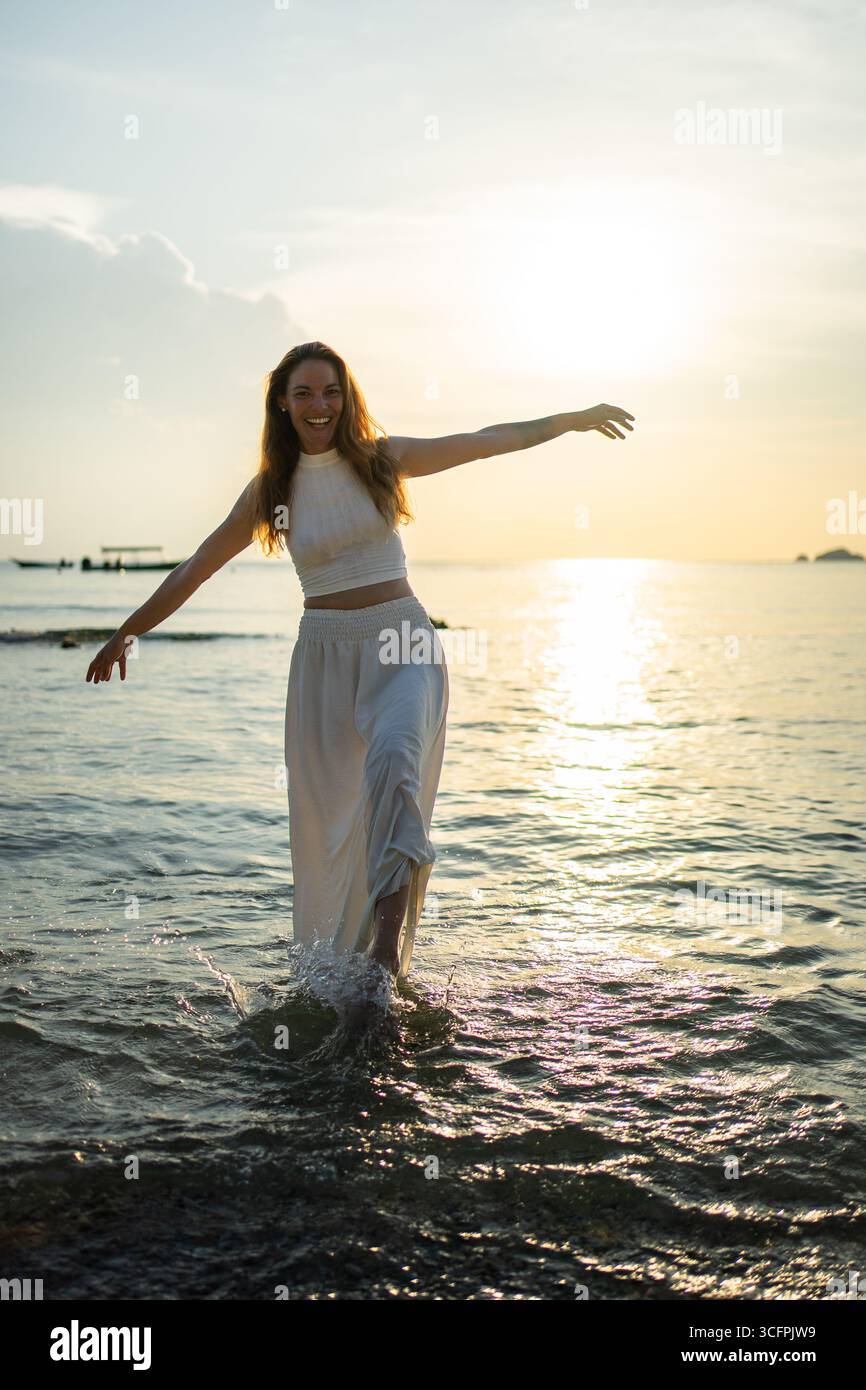 Young woman walking in the sea, enjoying the sunset and feeling happy and free Stock Photo
