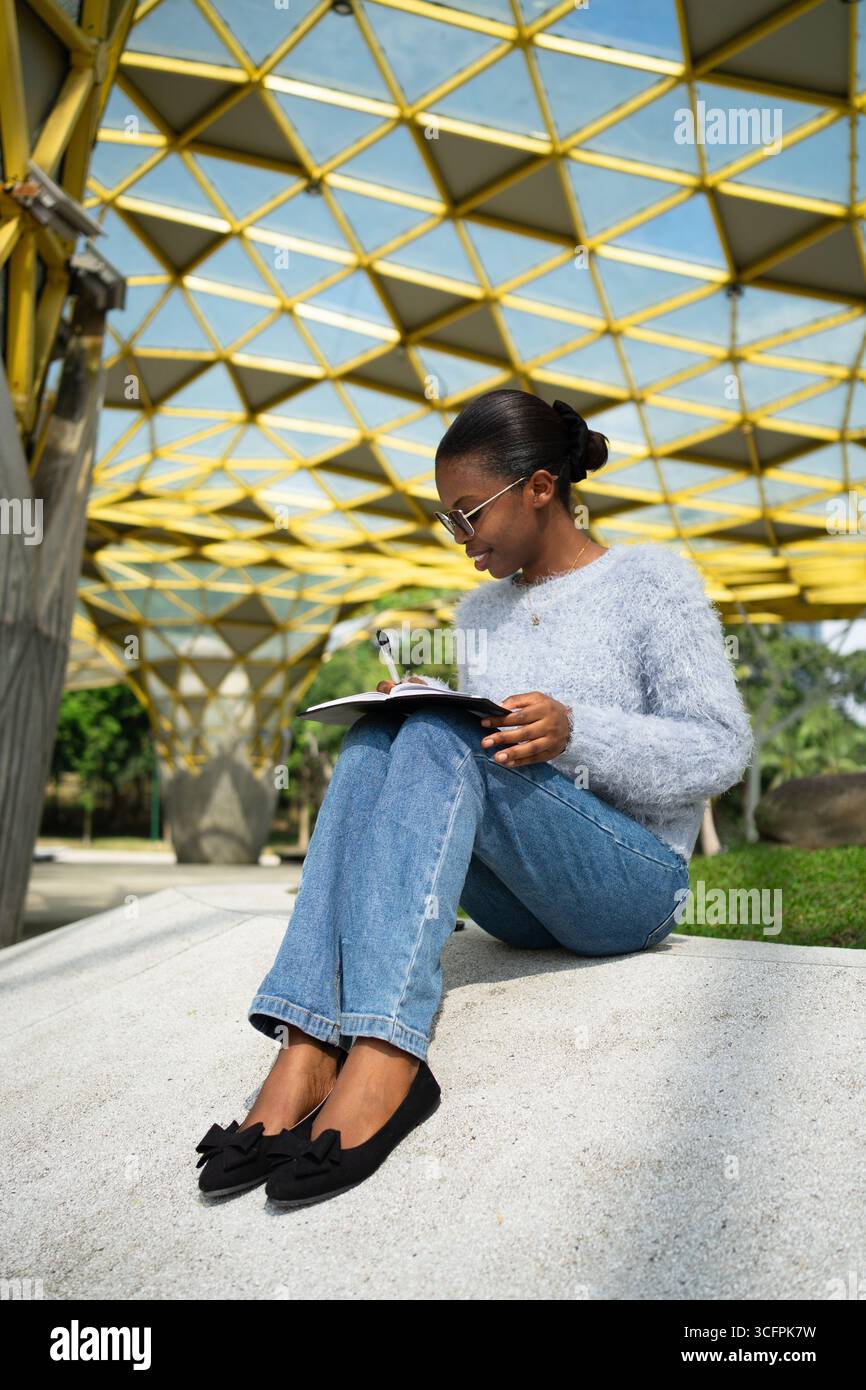 University student taking notes while sitting outdoors on campus Stock Photo