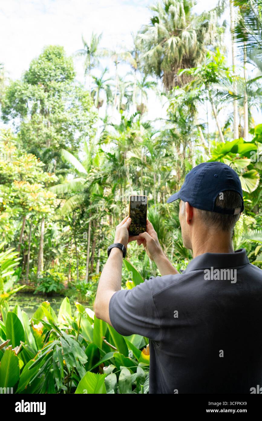 Tourist wearing a cap taking pictures of a tropical forest with his smartphone Stock Photo