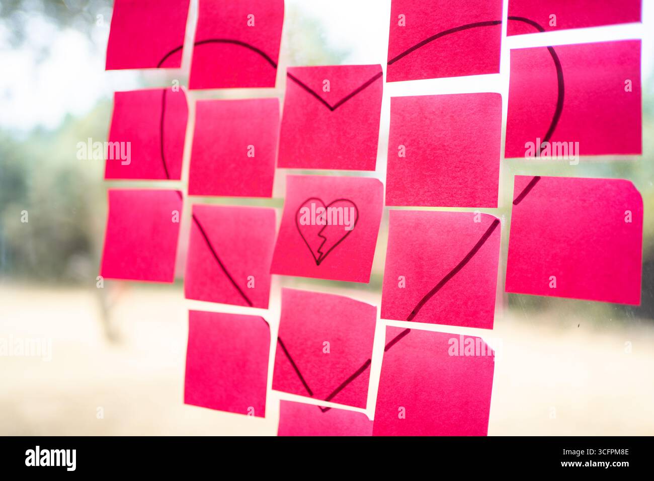 Pink sticky notes forming a heart shape with one note showing a broken heart, symbolizing a relationship breakup Stock Photo