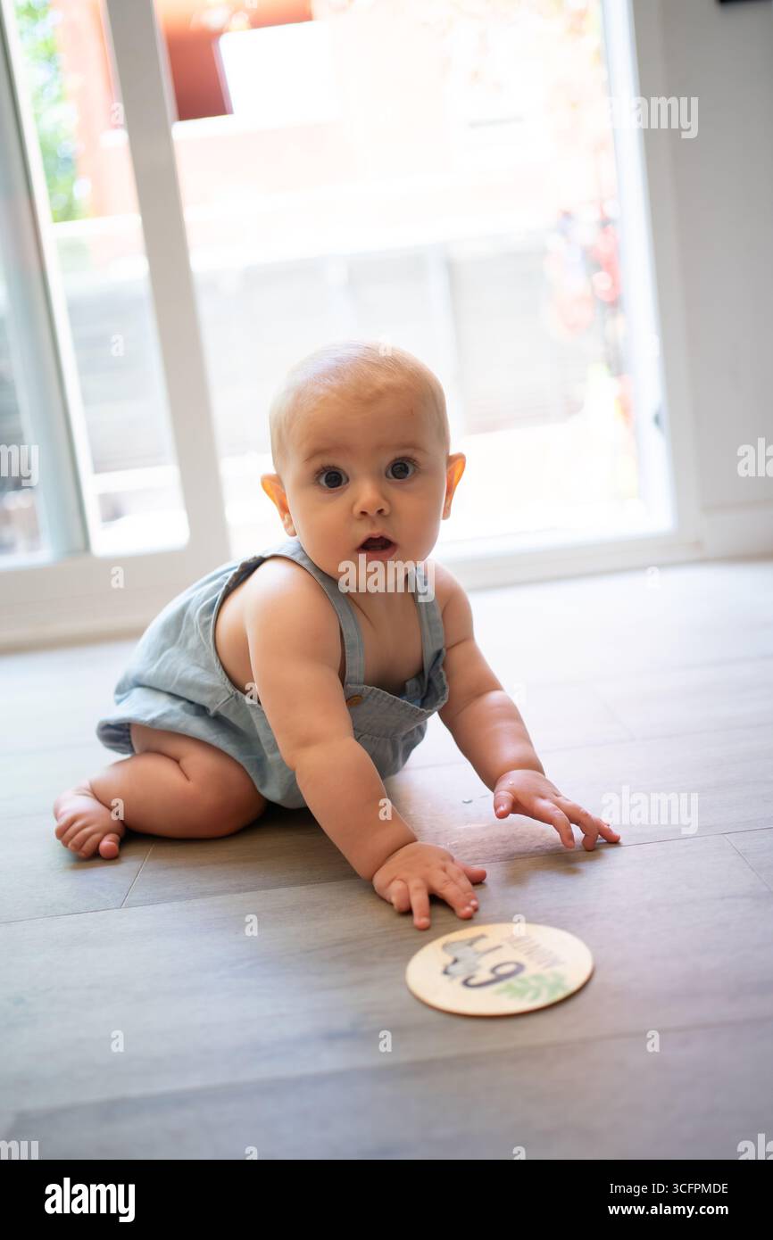 Adorable baby crawling towards a nine-month milestone card, marking a special moment in their development Stock Photo