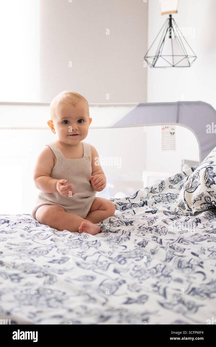 Adorable baby sitting on a bed, enjoying a peaceful moment Stock Photo