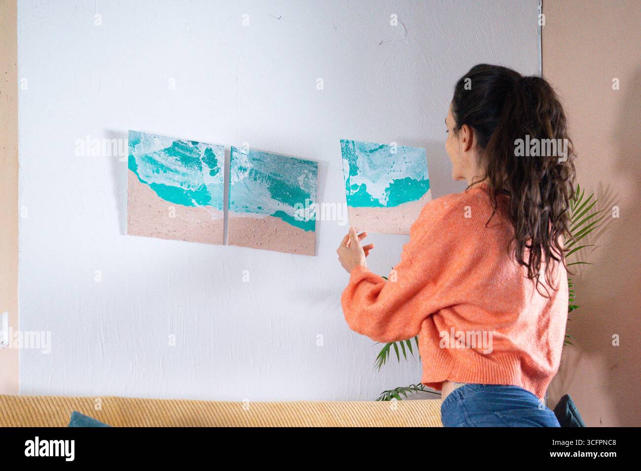 Woman hanging triptych painting of turquoise ocean waves on white wall Stock Photo