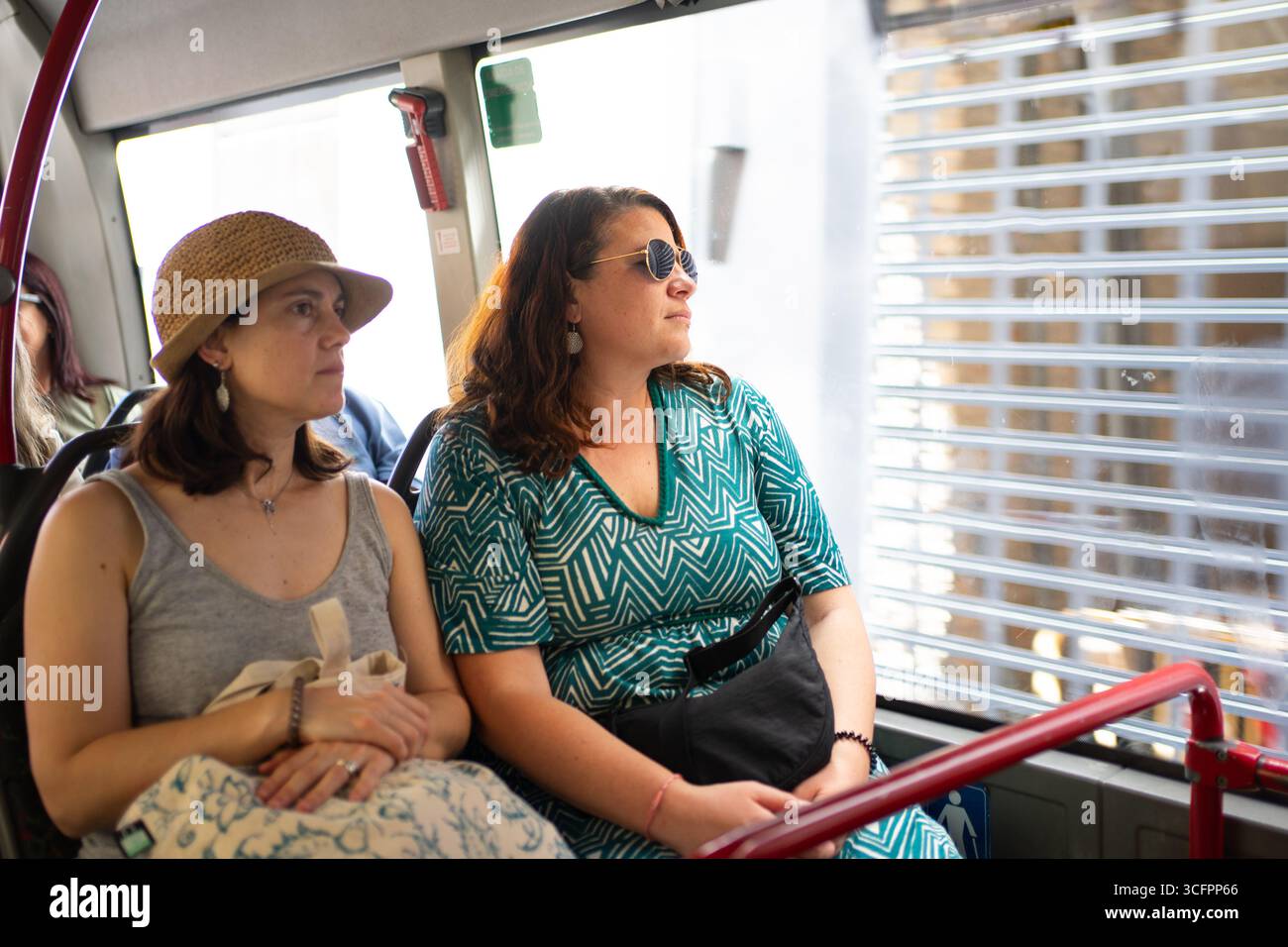 Two female tourists are sitting in a bus and admiring the city view through the window during their sightseeing tour Stock Photo