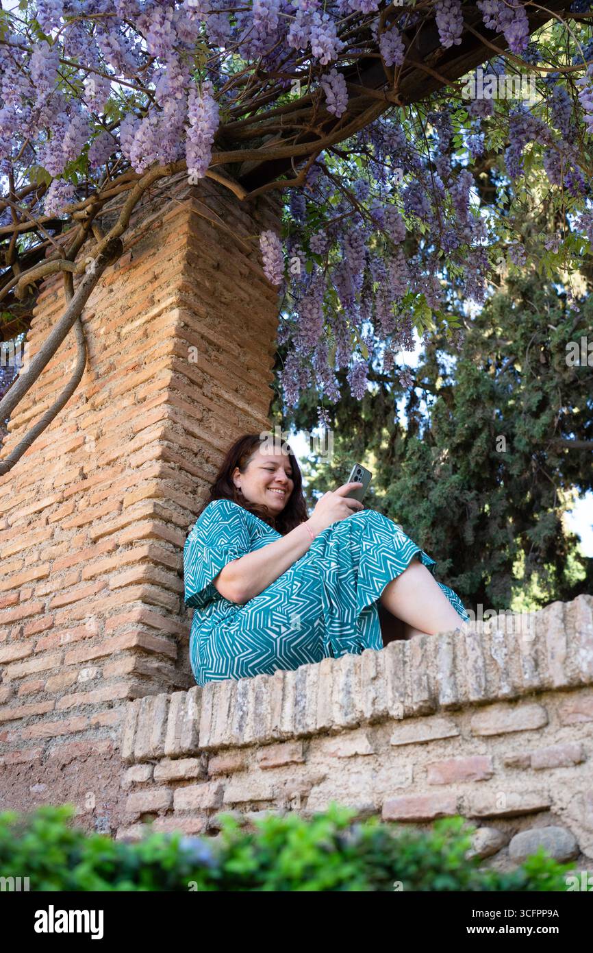 Woman using mobile phone under blooming wisteria Stock Photo