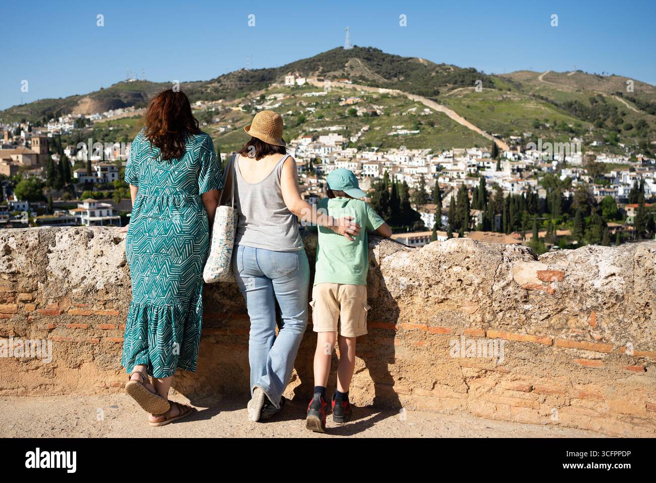Tourists admiring the cityscape of granada with its white houses, green hills, and clear blue sky Stock Photo