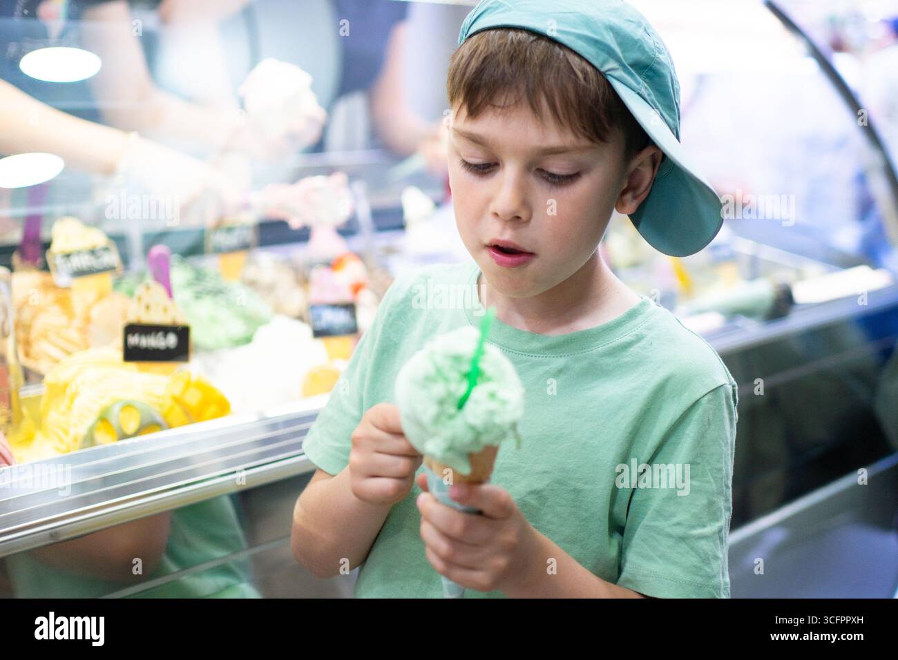 Young boy savoring a refreshing ice cream cone in front of a colorful gelato display Stock Photo