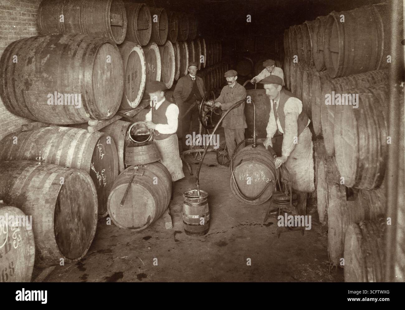 The wine cellars of a municipal trading depot. Workers pour or pump wine from large barrels into smaller ones. [Amsterdam, Netherlands], 1918..  Vintage Archive daily life Dutch Photograph, 1910s.   By Kees Hofker Stock Photo