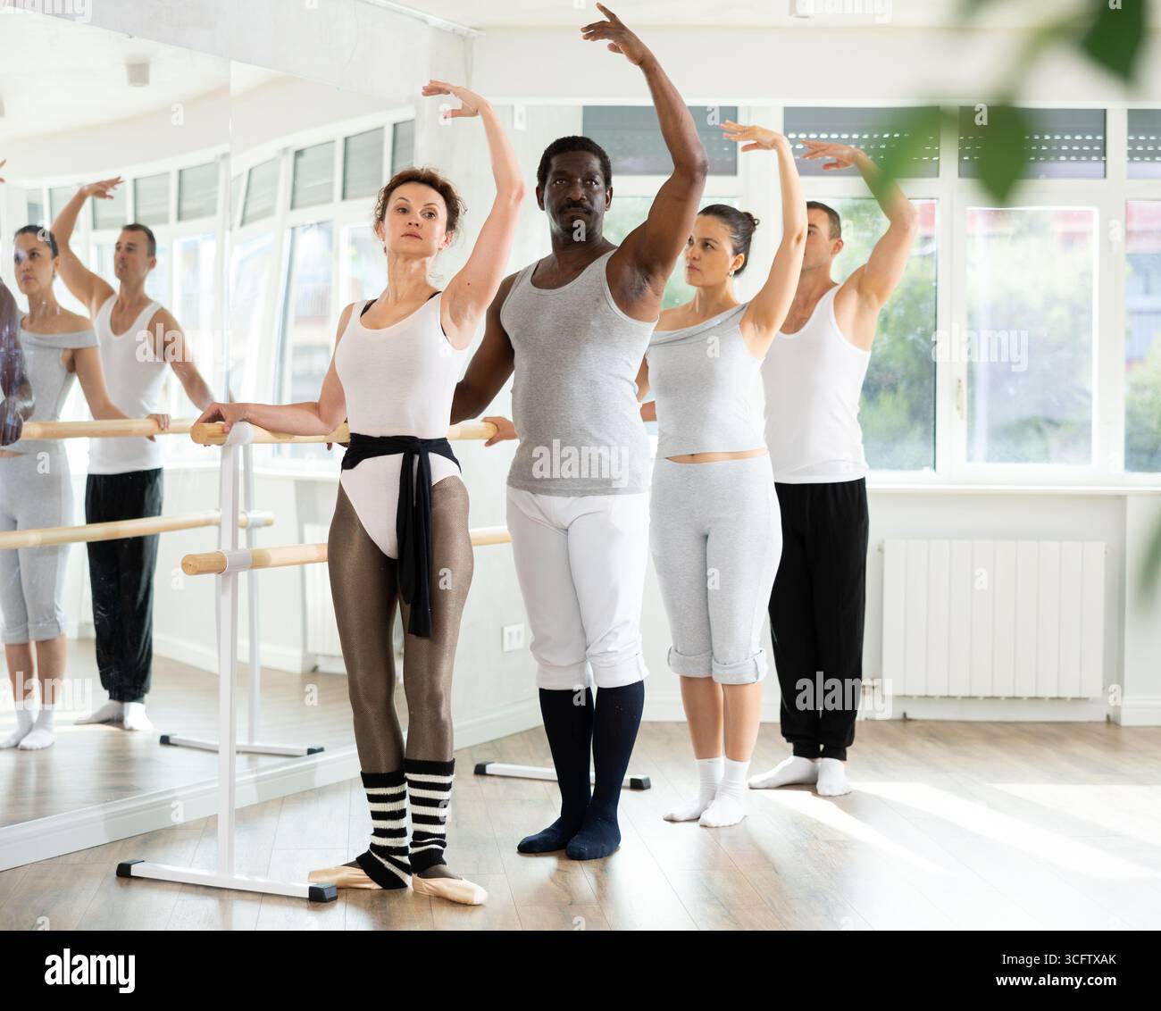 Group mastering third position at barre in ballet studio Stock Photo