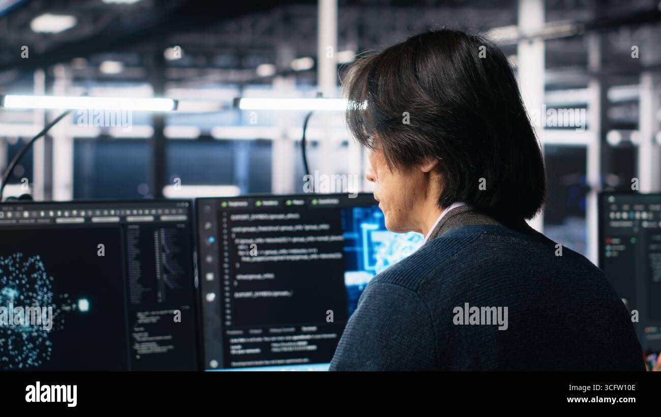 Technician arriving in data center office, coding with generative AI assistance. IT expert sitting at desk, starting work on artificial intelligence large language model solving tasks, camera A Stock Photo