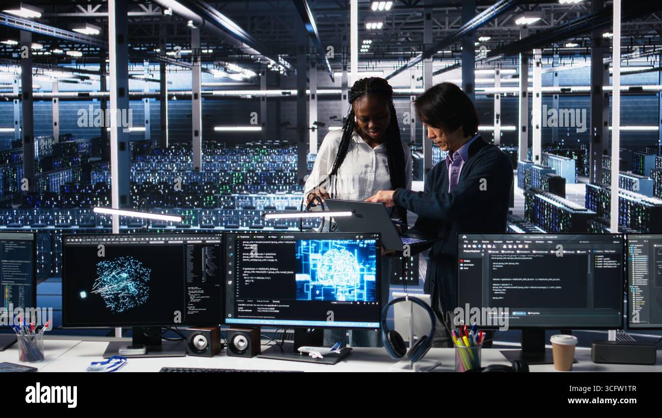 Team of data center engineers looking over paperwork and using deep learning algorithms to analyze datasets. Employees in multiethnic server farm using AI to recognize data patterns, camera A Stock Photo