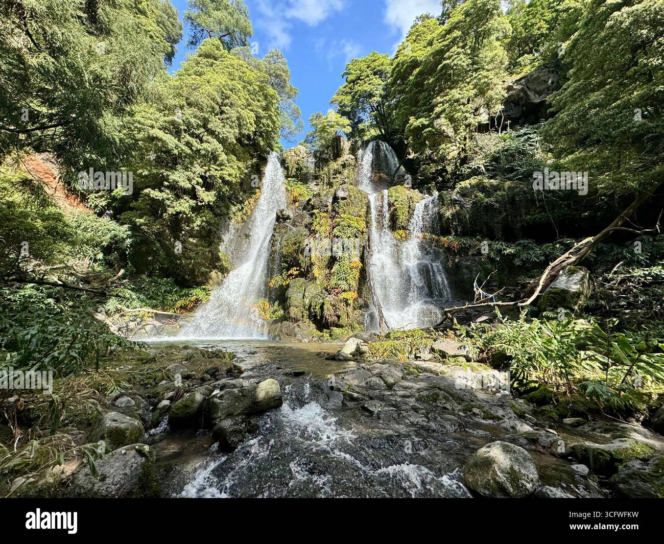 Waterfall along hiking trail PR39SMI in the Azores, Portugal, surrounded by lush greenery and volcanic rocks. - Smartphone Captured Stock Image