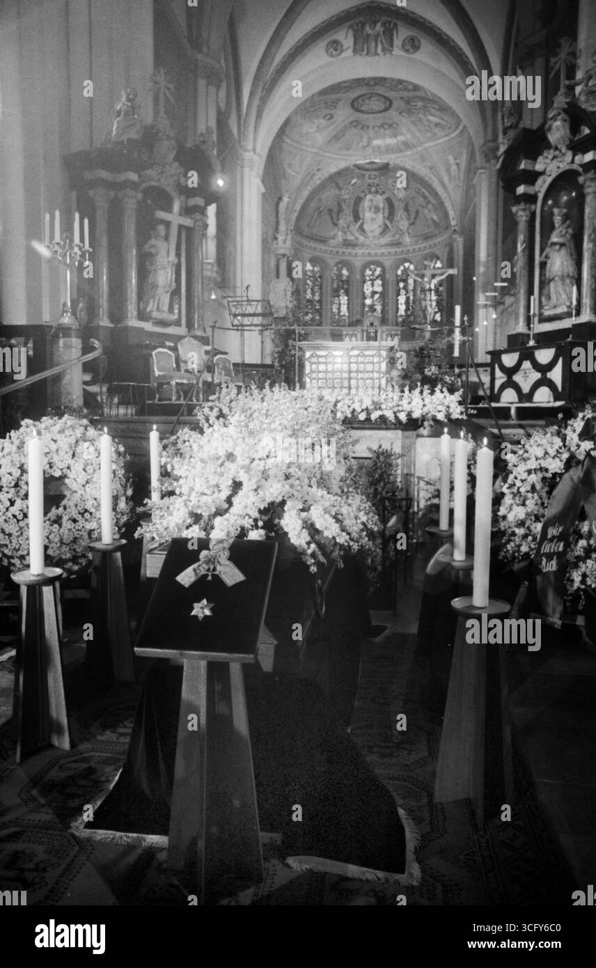 Sarg von Mildred Scheel ist im Bonner Münster feierlich aufgebahrt, umgeben von weißen Blumenkränzen und Kerzen. Im Vordergrund liegt das Bundesverdienstkreuz mit Stern auf Samt. Der festlich geschmückte Altarraum bildet den Hintergrund dieser zentralen Szene des Trauergottesdienstes. Stock Photo