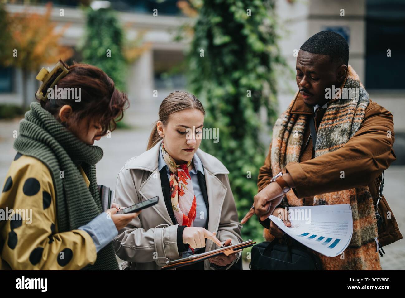 Multiracial Colleagues Collaborating Outdoors with Documents and Devices Stock Photo