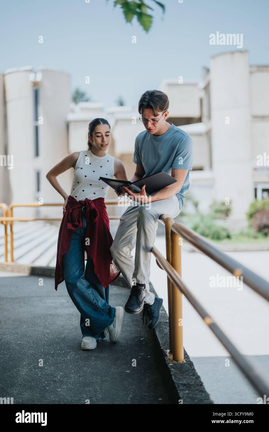 Two students discussing a project outdoors on a sunny college campus Stock Photo