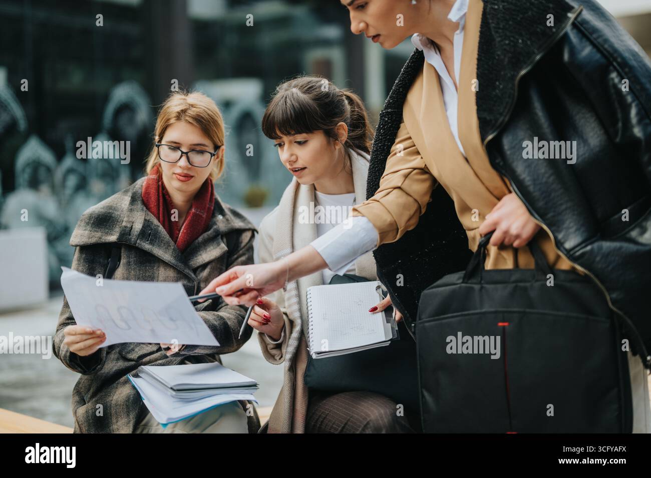 Three businesswomen collaborating outdoors while analyzing documents and notes together. Stock Photo