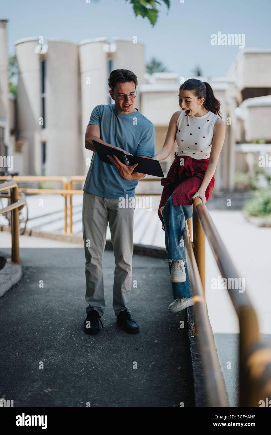 Two cheerful students reviewing documents outdoors during a pleasant day Stock Photo